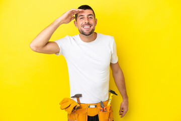 young electrician caucasian man isolated on yellow background looking far away with hand to look...