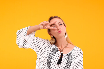 Portrait of hippie woman showing peace sign on yellow background