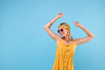 Portrait of smiling hippie woman in sunglasses dancing on light blue background. Space for text