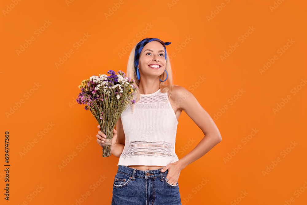 Wall mural Happy hippie woman with bouquet of flowers on orange background. Space for text