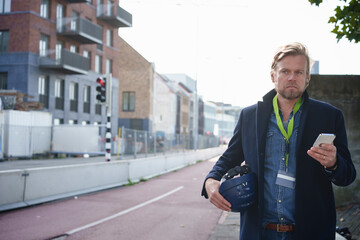 Architect holding hardhat and smart phone at street near buildings
