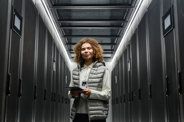 Smiling engineer with tablet PC standing in server room