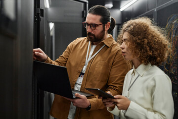 IT professionals examining servers with laptop and tablet PC in data center