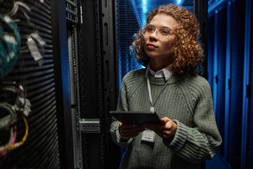 Young IT engineer examining supercomputer equipment and holding tablet PC in data center