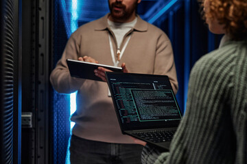 IT professionals working and discussing over data on laptop in server room
