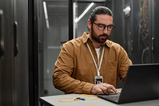 IT professional using laptop in server room at desk