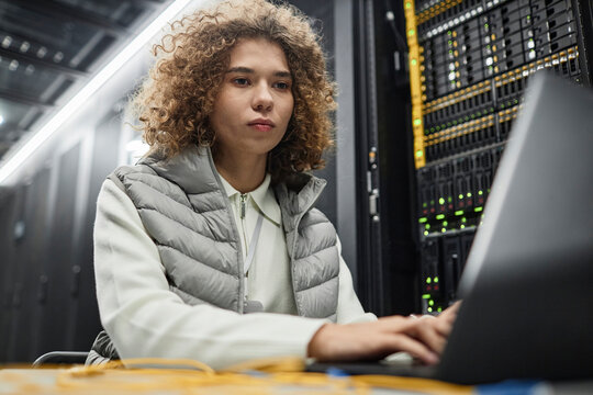 Engineer with curly hair working on laptop in server room