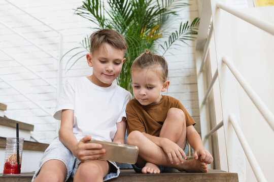 Brothers watching smart phone sitting on staircase at home
