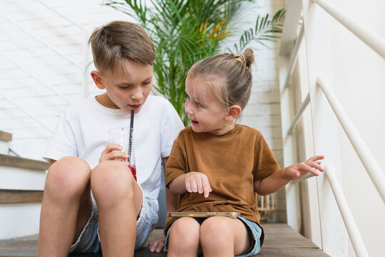 Boy with mobile phone talking to brother drinking juice at home