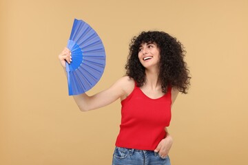Happy woman holding hand fan on beige background
