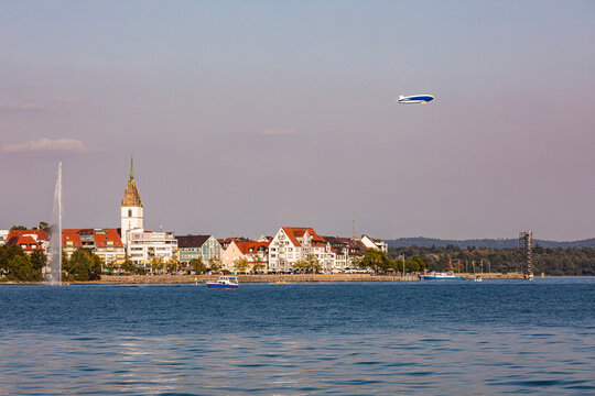 Germany, Baden-Wurttemberg, Friedrichshafen, Blimp flying over city on shore of lake Bodensee at dusk