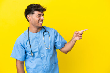 Young surgeon doctor man isolated on yellow background pointing finger to the side and presenting a...