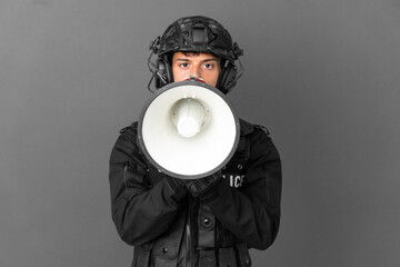 SWAT caucasian man isolated on grey background shouting through a megaphone