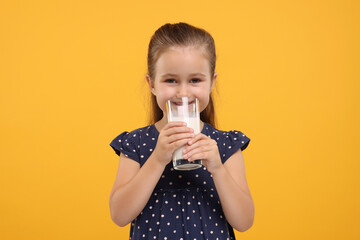 Cute girl with glass of fresh milk on orange background