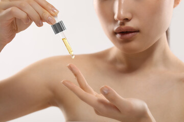 Beautiful young woman applying cosmetic serum onto her finger on white background, selective focus