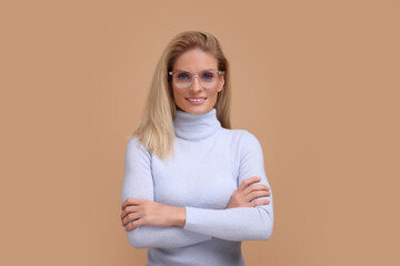 Fototapeta premium Portrait of smiling middle aged woman in glasses with crossed arms on beige background