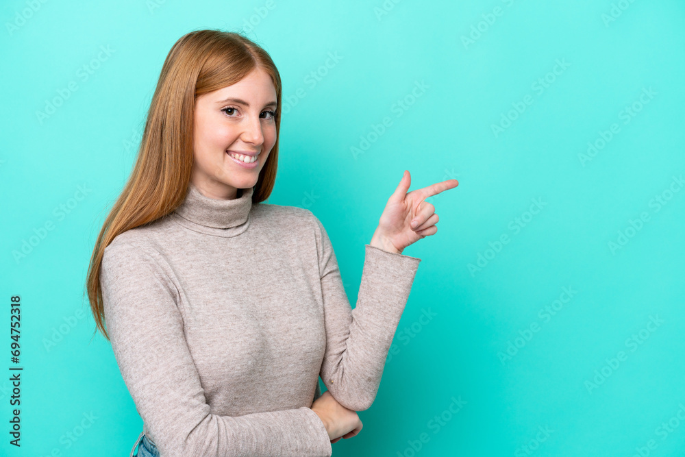 Poster Young redhead woman isolated on blue background pointing finger to the side