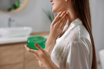 Obraz na płótnie Canvas Young woman applying aloe gel onto her neck in bathroom, closeup