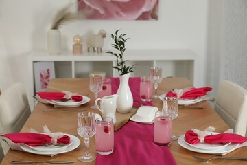 Color accent table setting. Glasses, plates, pink napkins and vase with green branch in dining room