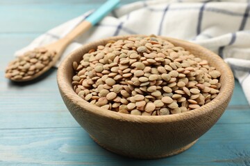 Raw lentils in bowl on light blue wooden table, closeup