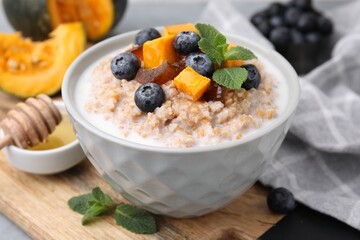 Tasty wheat porridge with pumpkin, dates and blueberries in bowl on table, closeup