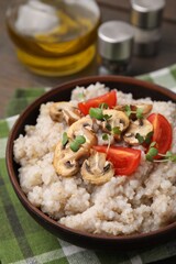 Delicious barley porridge with mushrooms, tomatoes and microgreens in bowl on table, closeup