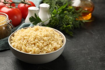 Delicious bulgur in bowl on black table, space for text