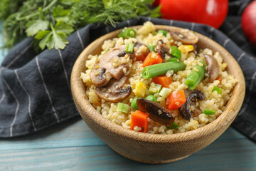 Delicious bulgur with vegetables and mushrooms on light blue wooden table, closeup