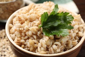 Delicious pearl barley with parsley in bowl on table, closeup