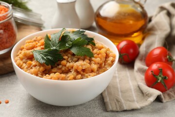 Delicious red lentils with parsley in bowl and products on light grey table, closeup