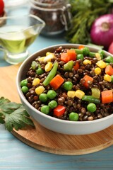 Delicious lentils with vegetables in bowl and parsley on light blue wooden table, closeup