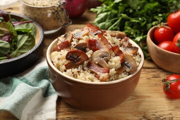 Tasty quinoa porridge with fried bacon and mushrooms in bowl on wooden table, closeup
