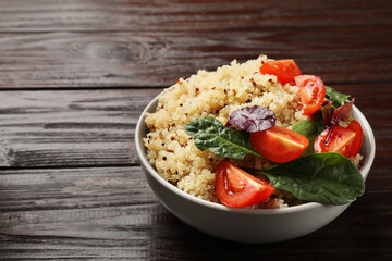 Tasty quinoa porridge with tomatoes and spinach in bowl on wooden table, closeup. Space for text