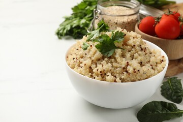Tasty quinoa porridge with parsley in bowl on white table, closeup. Space for text