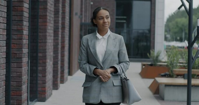 Dolly shot of elegant African American businesswoman walking in city street smiling looking around. Businessperson and urban lifestyle concept.