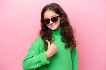 Fototapeta premium Little caucasian girl wearing sunglasses isolated on pink background with thumbs up because something good has happened
