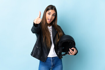 Young caucasian woman holding a motorcycle helmet isolated on blue background with thumbs up...