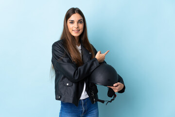 Young caucasian woman holding a motorcycle helmet isolated on blue background pointing back