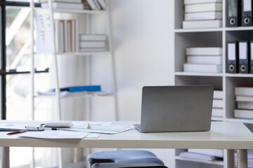 Laptop Computer, notebook, and eyeglasses sitting on a desk in a large open plan office space after working hours	