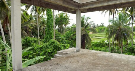 Walk through an unfinished villa, beautiful view of tropical thickets in small ravine seen ahead. First person view camera moves forward through the empty concrete frame of multi-floor building