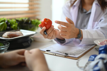 Cropped shot of female nutritionist holding a tomato while giving consultation to patient in clinic.