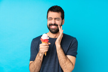 Young man with a cornet ice cream over isolated blue background with toothache