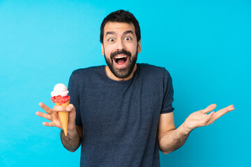 Young man with a cornet ice cream over isolated blue background with shocked facial expression
