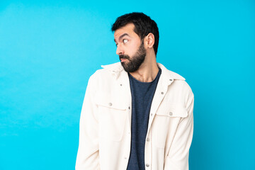 Young handsome man with white corduroy jacket over isolated blue background making doubts gesture looking side