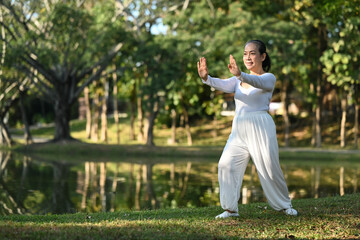 Full length of smiling senior woman practicing Qigong near lake during sunrise.