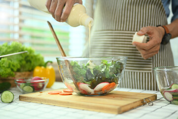 Cropped shot senior man pouring sauce on a fresh salad. Healthy eating and culinary concept .