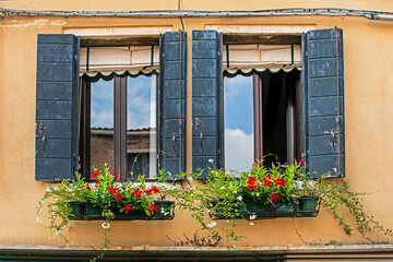 Fototapeta na wymiar beautiful old windows with a balcony with fresh geranium flowers in Venice