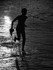 Isolated portrait of a young girl running and playing on the water edge of the sea during sunset-...