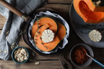 Fresh pumpkin slices with aromatic thyme and garlic in frying pan on wooden table, flat lay