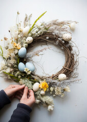 Fototapeta na wymiar A florist's hands caught in the act of crafting an Easter wreath, with fingers gracefully positioning speckled pastel eggs among a bed of soft greenery on a pale oak background